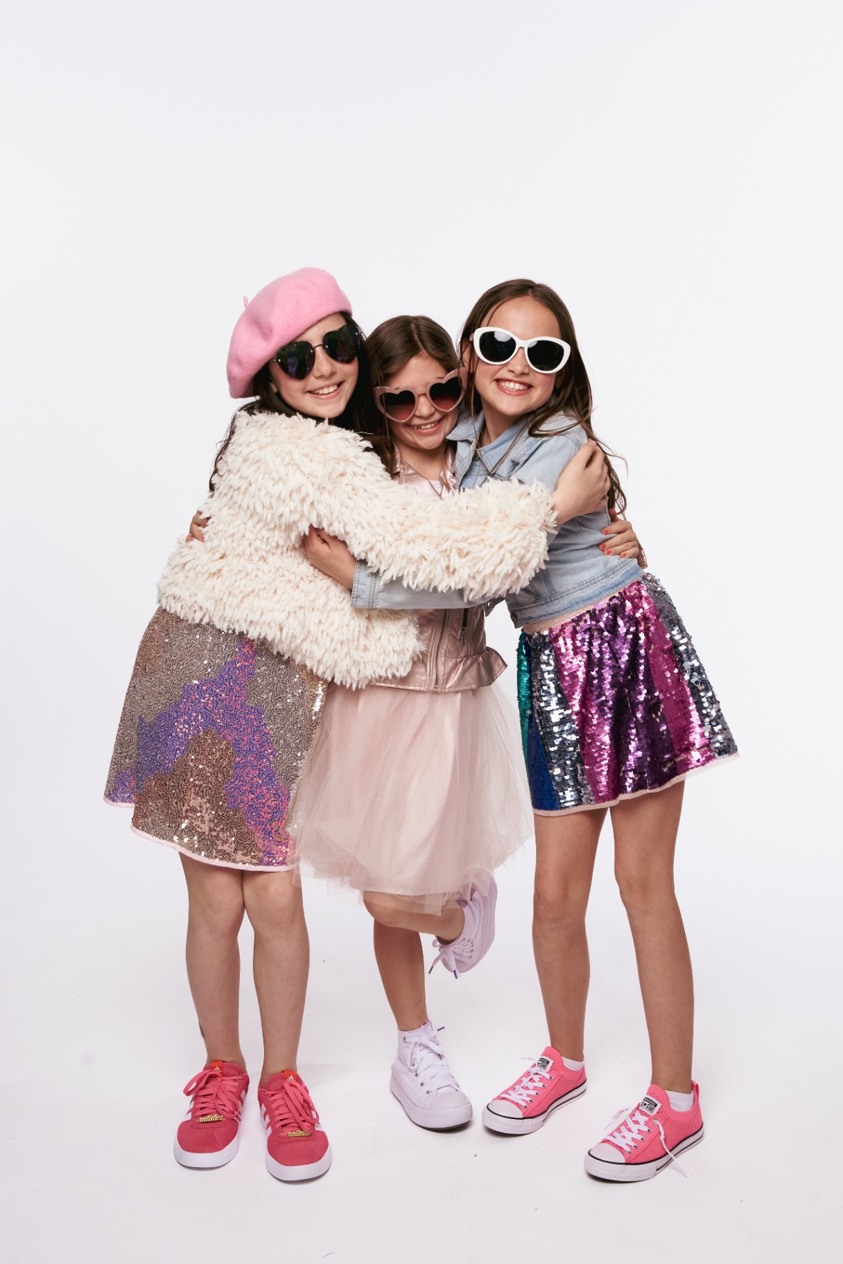 Three students hugging in editorial outfits against a white backdrop